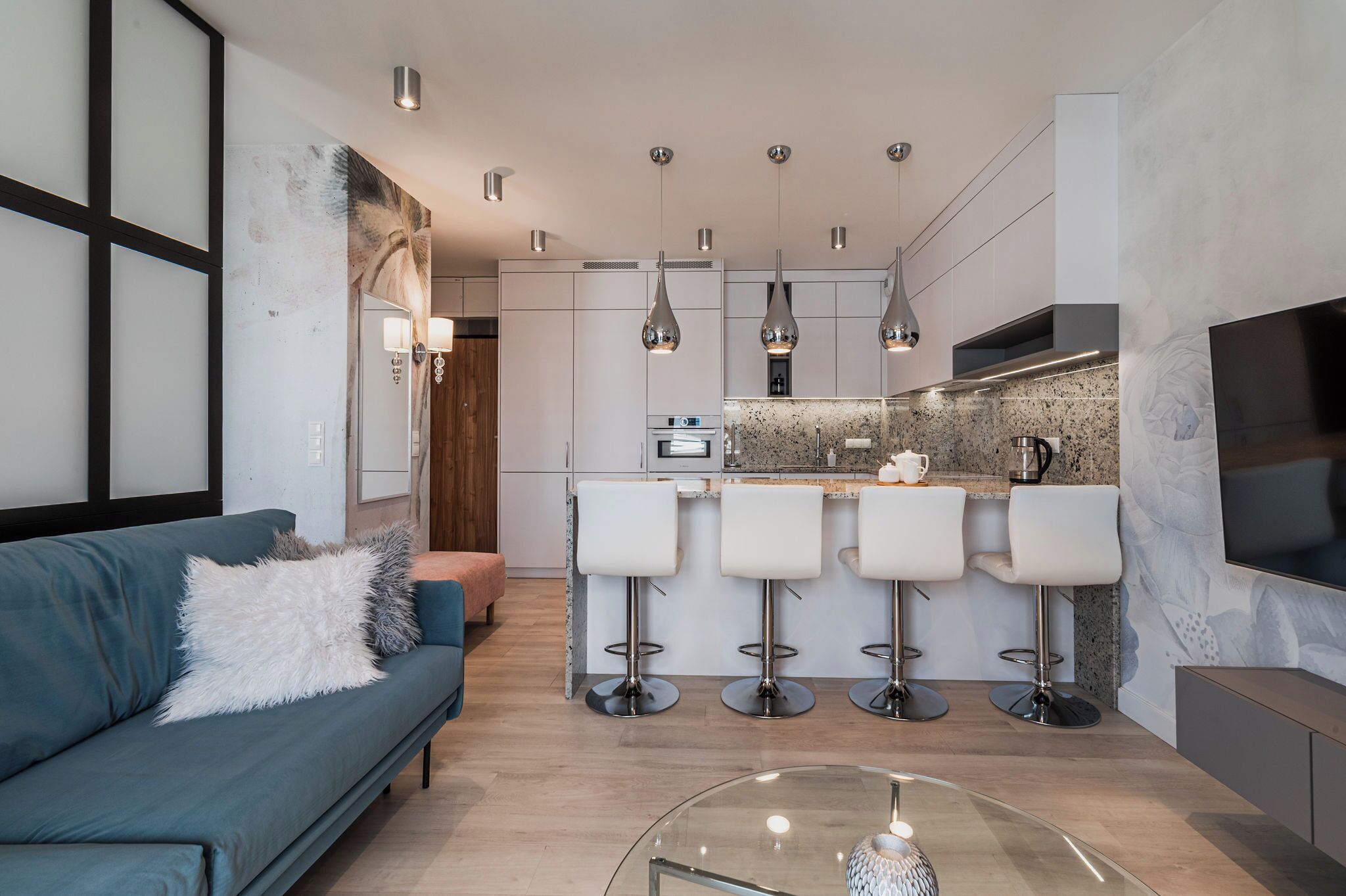 Une cuisine moderne dotée d’un îlot central, de tabourets de bar, de luminaires suspendus et d’un téléviseur à écran plat.