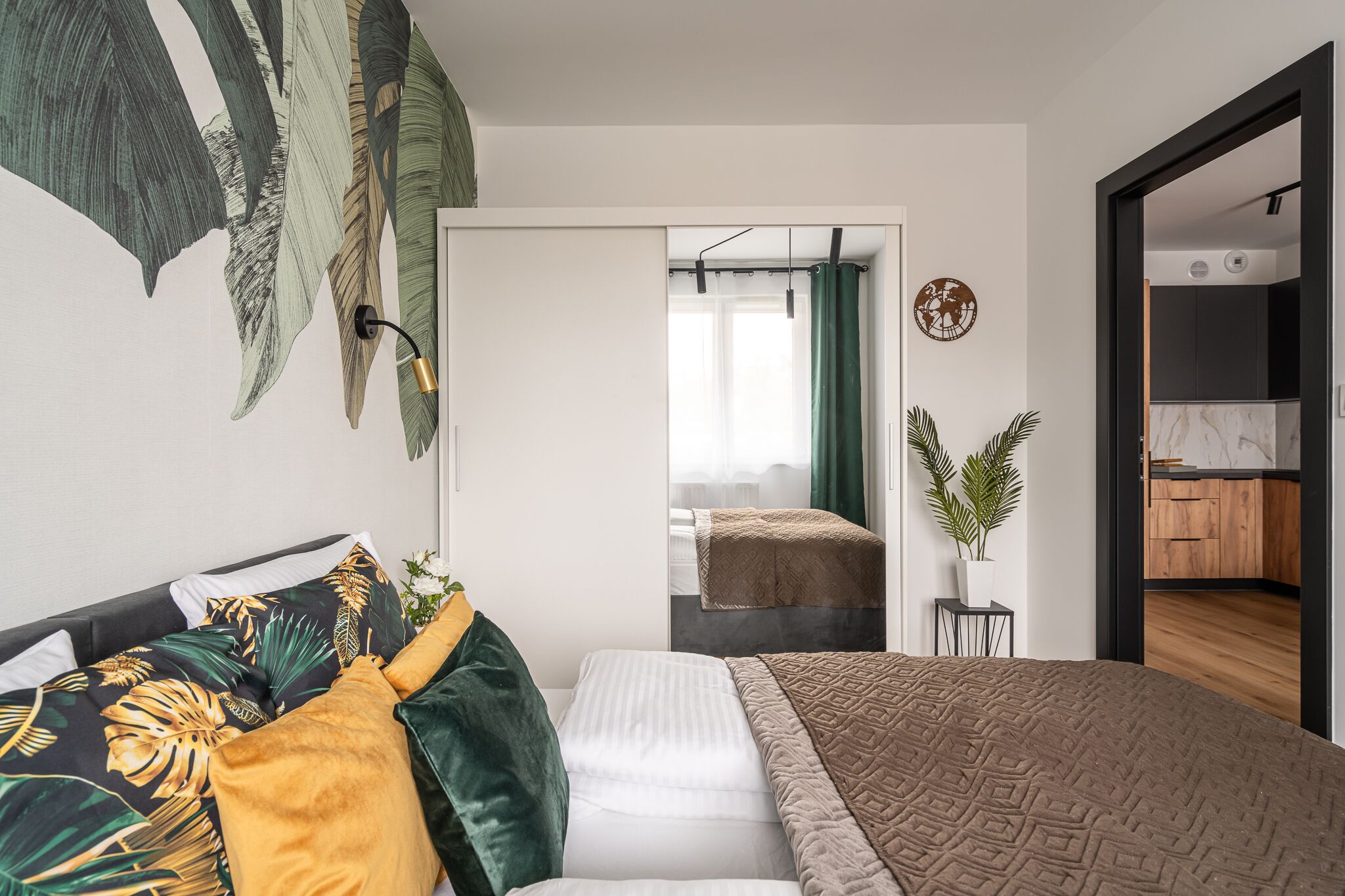 A modern bedroom with a bed, a sofa, and a view into a kitchen.
