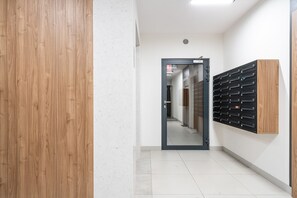 Un pasillo con una puerta de madera, un buzón en la pared y suelo de baldosas.