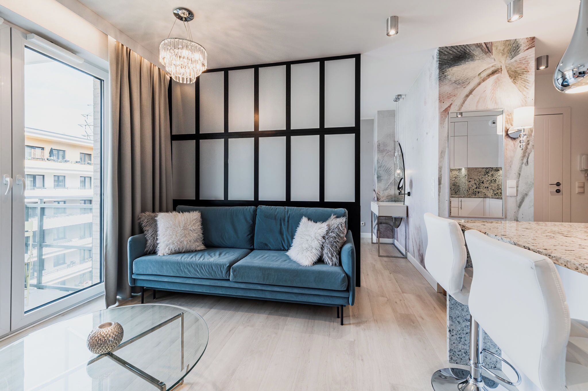 A modern living room with a blue sofa, a glass coffee table, and a view of the city through large windows.