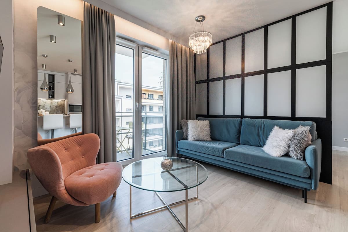 A modern living room with a glass coffee table, a blue sofa, and a pink armchair.