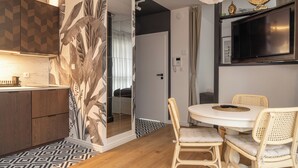 A modern kitchen with a large mirror, a dining area with wicker chairs, and a flat-screen TV mounted on the wall. - RentPlanet - Apartament Długa (Wroclaw)