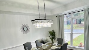 Ein Esszimmer mit einer Chandelüster, einem für sechs Personen gedeckten Esstisch und Blick ins Freie durch ein großes Fenster.
