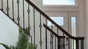 Eine Treppe mit Holzgeländer und schwarzen Spindeln, die zu einer weißen Tür mit Glasfenster führt.