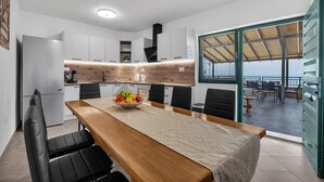 Une cuisine moderne avec des meubles blancs, un plan de travail en bois et un coin repas comprenant une table en bois et des chaises noires.