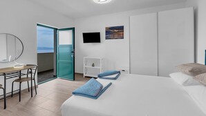 Une chambre d’hôtel avec un lit, un bureau et une chaise, une télévision, un tableau et une vue sur la mer.