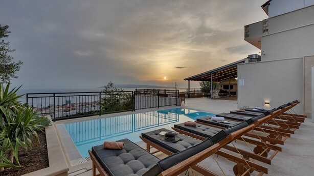 Une piscine sur le toit, agrémentée de chaises longues, offrant une vue sur le coucher du soleil et un panorama de la ville en arrière-plan.