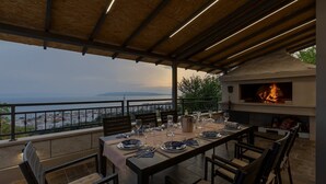 Un espace extérieur aménagé pour les repas, avec vue sur la mer, un barbecue et une table dressée pour quatre personnes.