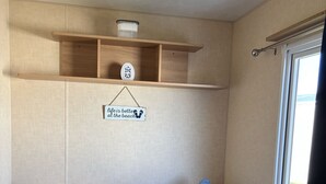 A compact room with two beds, a shelf with a decorative item, a sign, and a window.