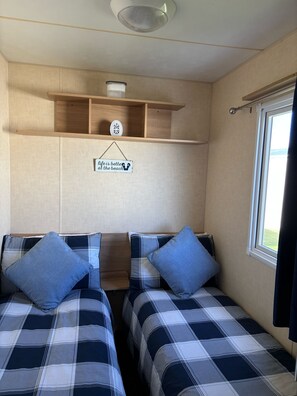 A compact room with two beds, a shelf with a decorative item, a sign, and a window.