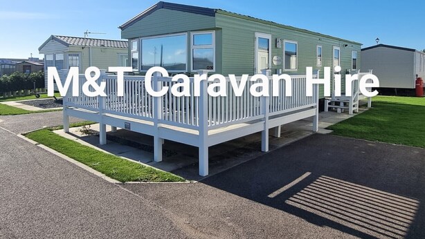 A mobile home with a fenced porch, a small attached garage, and a well-maintained lawn. - Luxury 8 berth spacious caravan  (Chapel Saint Leonards)