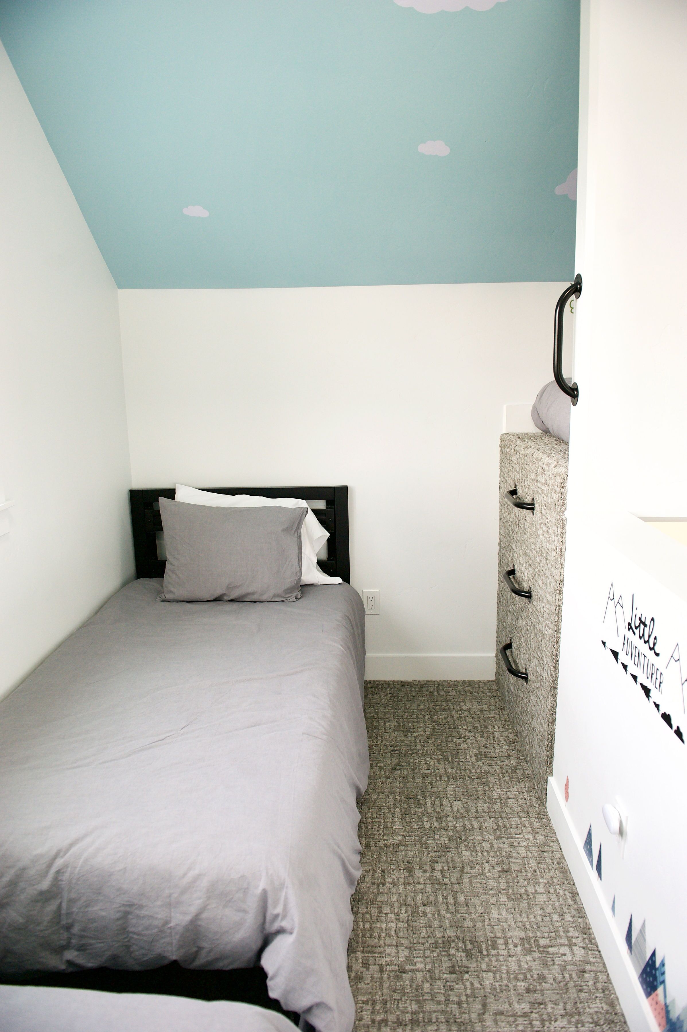 Un dormitorio pequeño y ordenado con cama, cómoda y una pared con diseño de nubes.