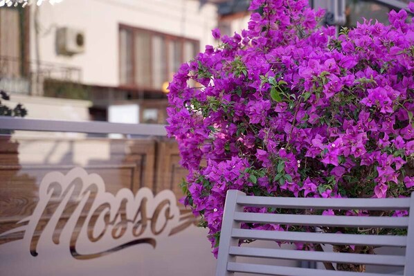 A white chair with a large, purple flower arrangement in front of a sign with the word "Moss" in cursive. - Mosso Boutique Hotel (Ula)