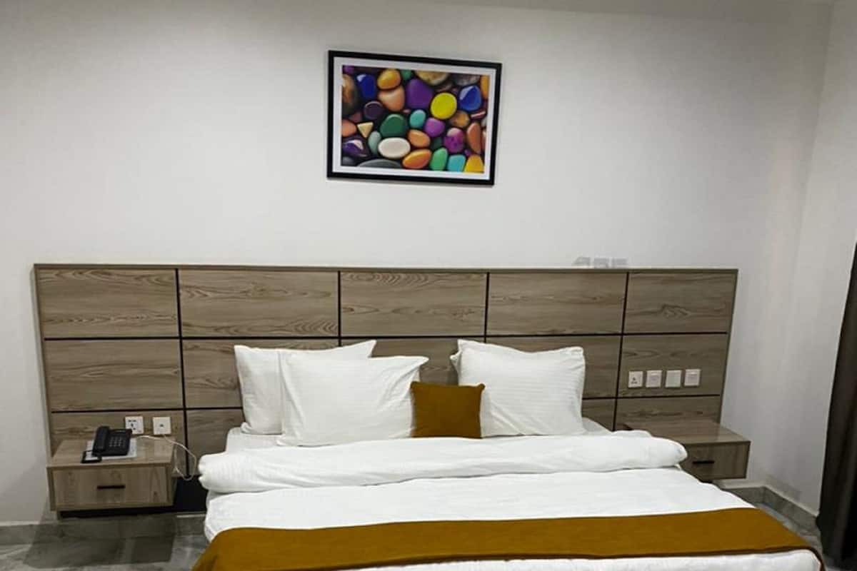 Un dormitori modern amb un llit gran, una tauleta de nit, un telèfon fixat a la paret i un quadre abstracte i colorat penjat sobre el llit.