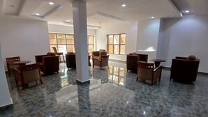 A spacious lobby with a polished marble floor, several wooden chairs and tables, and large windows allowing natural light.