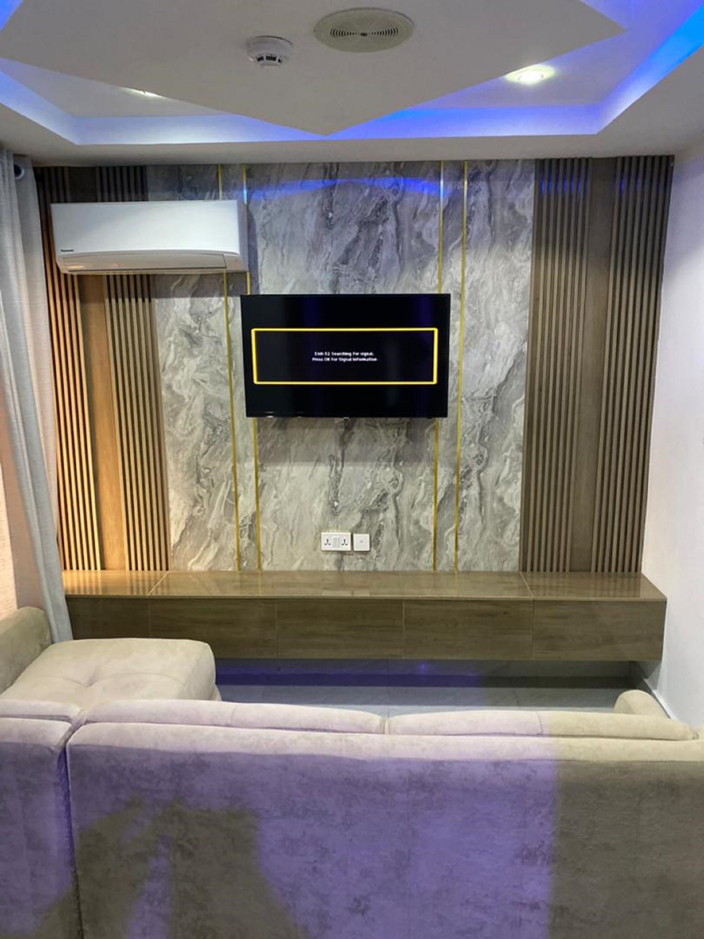 A modern living room with a flat-screen TV mounted on a marble wall, a built-in bench, and recessed ceiling lighting.