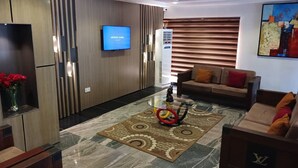 A modern living room with a flat-screen TV mounted on the wall, a sofa, a coffee table with a decorative item, and a patterned rug.