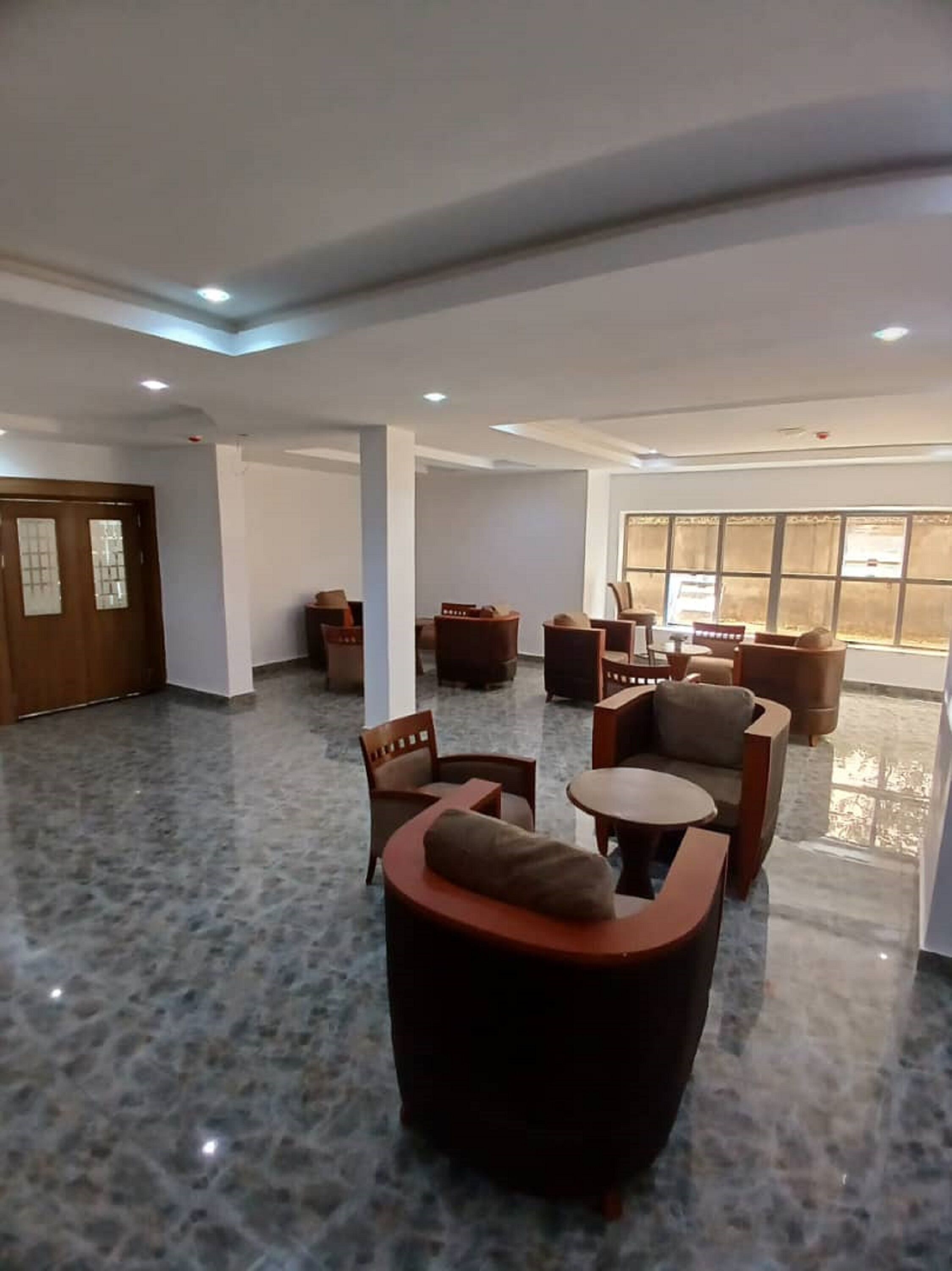 A spacious lobby with a marble floor, several seating areas including sofas and chairs, and a large window providing natural light.