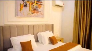 A hotel room with a bed, a nightstand, a painting on the wall, and a window with curtains.