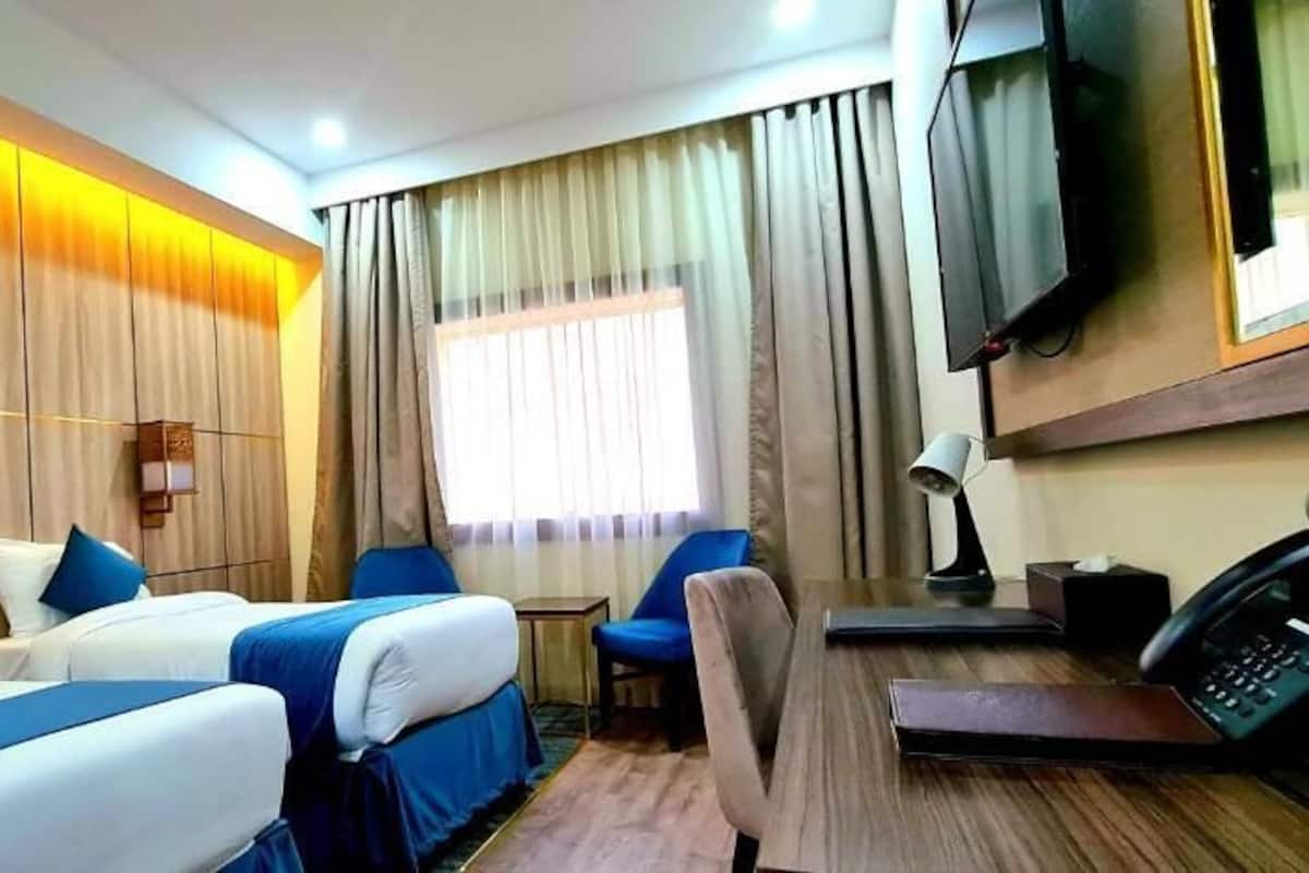 A hotel room with two beds, a desk, a chair, a TV, and a window with curtains.