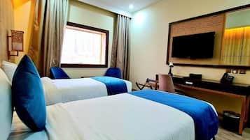 Een hotelkamer met twee bedden, een bureau, een stoel, een televisie en een raam met gordijnen.