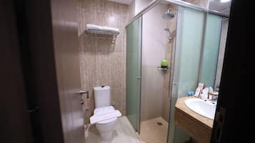 Un baño moderno con ducha envuelta en vidrio, inodoro y lavamanos con artículos de aseo.