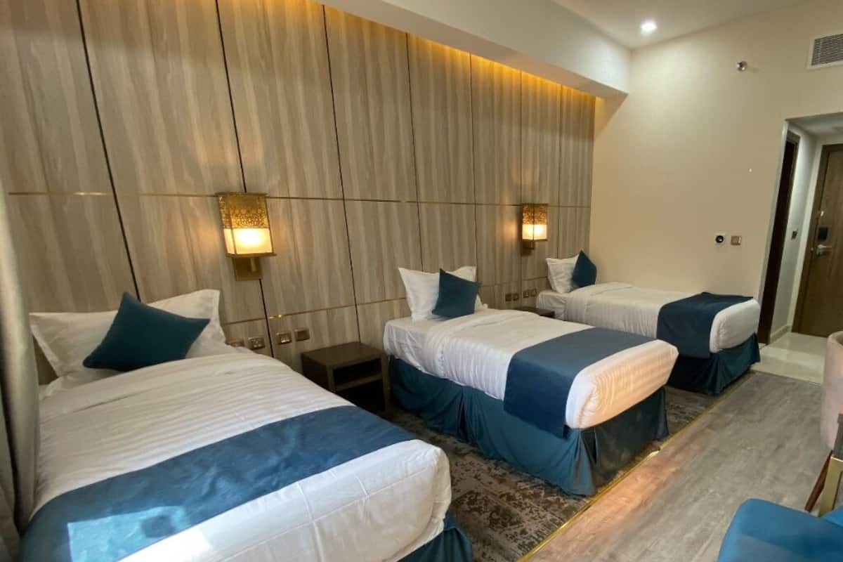 A hotel room with three beds, each with white linens and teal accents, and two wall-mounted lamps.