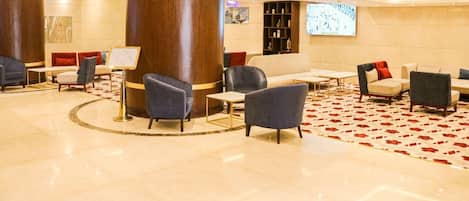 A lobby with a circular seating area, a large pillar, and a carpet with a red pattern.