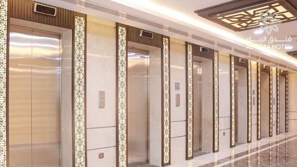 A hotel corridor with multiple elevators, each with a decorative panel and a digital display above the doors. - Al Ebaa Hotel (Makkah)
