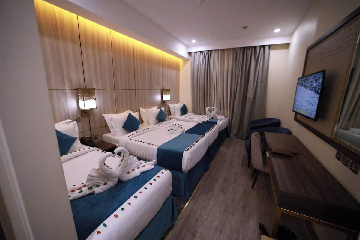A hotel room with three beds, a desk, and a television.
