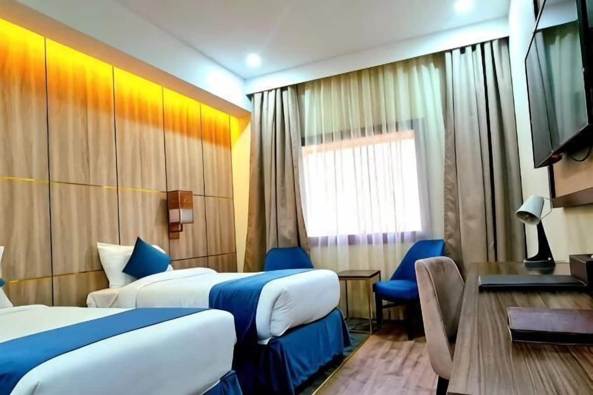 A hotel room with two beds, a desk, a chair, a TV, and a window with curtains.