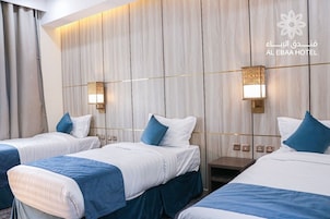 Habitación de hotel con tres camas, cada una con ropa de cama blanca y azul, y dos lámparas de pared.