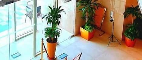 Un hall d’entrée agrémenté d’un lustre moderne, de plantes en pot et d’une entrée en verre donnant sur un espace extérieur.