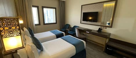 Une chambre d’hôtel avec deux lits, un bureau, une chaise, une télévision et un élément décoratif mural.