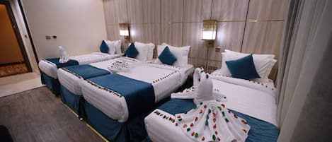 Une chambre d’hôtel avec trois lits alignés, chacun étant doté de draps blancs et de touches de couleur bleue.