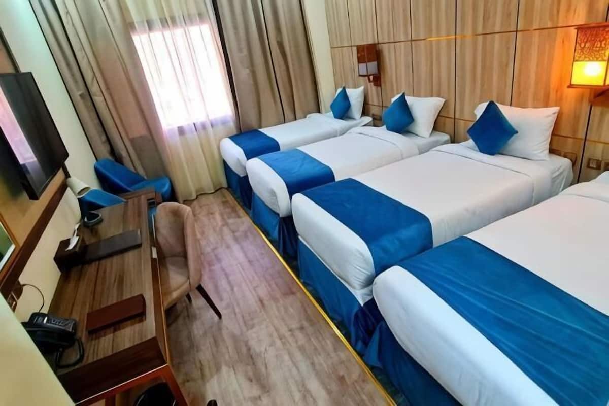 A hotel room with three beds, a desk, a chair, a TV, and a window with curtains.