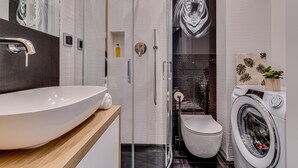 A modern bathroom with a large white sink, a glass-enclosed shower, a toilet, and a front-loading washing machine. - RentPlanet - Lokum Vena (Wroclaw)