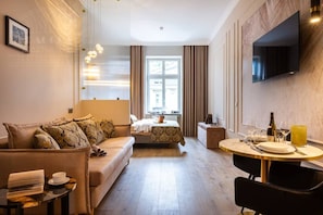 Ein modernes Hotelzimmer mit einer Couch, einem kleinen Tisch, einem an der Wand befestigten Fernseher und einem Fenster mit Vorhängen.
