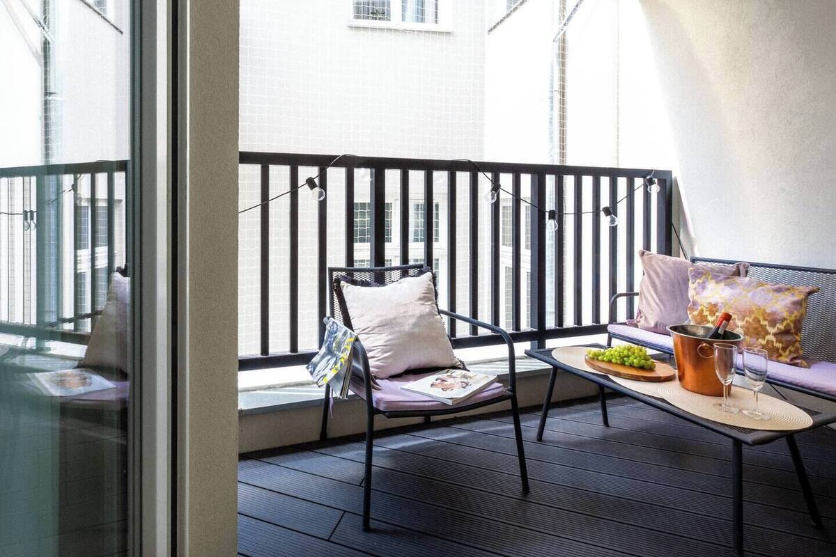 Un balcon avec une chaise, une table avec un seau de raisins et une bouteille, et un canapé avec des coussins.