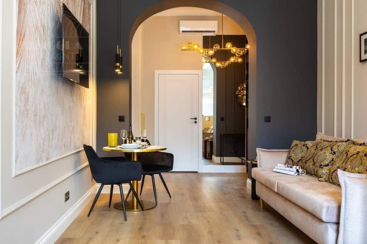 Un salon moderne comprenant un canapé, une table à manger avec des chaises, un téléviseur fixé au mur et un lustre.