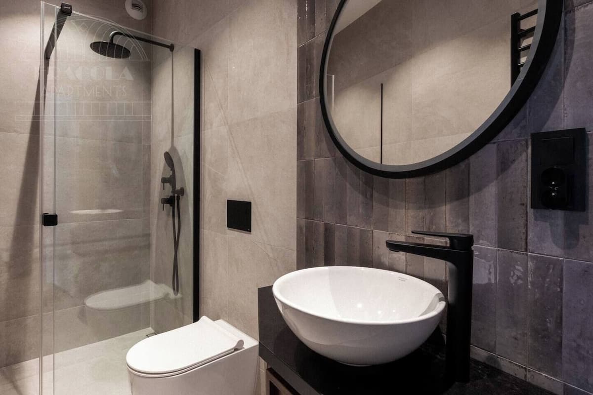Une salle de bain moderne avec une douche à parois de verre, un lavabo blanc et un miroir rond.