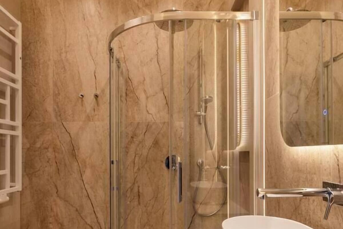 A bathroom with a glass-enclosed shower, a white sink, and a marble-tiled wall.