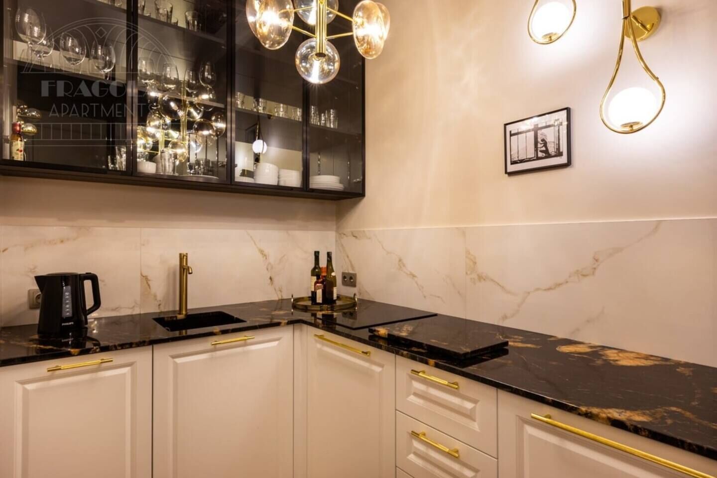 A kitchen with a black countertop, white cabinets, gold handles, a coffee maker, and a wine bottle.