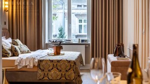 Une chambre d’hôtel avec un lit, une petite table, une fenêtre avec des rideaux et une bouteille de vin.