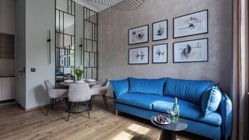 Una sala de estar moderna con un sofá azul, una mesa de comedor con sillas, y una cocina visible a través de un separador de vidrio.