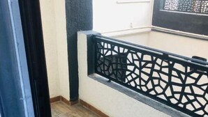 Un balcon doté d’une balustrade à motifs, d’un plancher en bois et offrant une vue sur un immeuble avec une fenêtre et une porte.