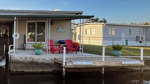 A house with a dock extending into a body of water, featuring a small patio with red chairs and a table.