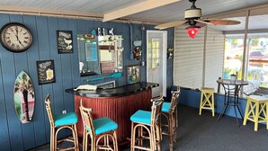 A bar area with a wooden counter, bar stools, a clock, and various wall decorations.