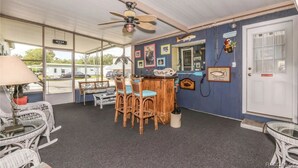 A room with a bar area, wicker furniture, and a ceiling fan.