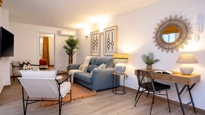 Una sala de estar moderna con un sofá, una mesa de centro, un escritorio con una silla, un televisor y cuadros en la pared.